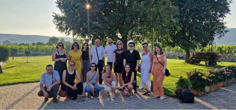 Grupa učesnika obuke pozira na otvorenom u uređenom zelenom okruženju, s drvećem i vinogradima u pozadini.